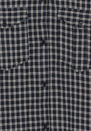 Navy ja valge ruuduline flanellist särk, millel on kaks rinna taskut, nööbid ees ja mustad nööbid, esitades pehme ja tekstureeritud kangast.