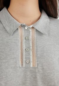 Grijze polo shirt met een kraag, vijf knopen en een kanten accent dat in het midden loopt. Zachte stof met een gladde textuur.