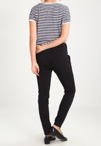 Pruhované námořnické modré a bílé tričko s krátkými rukávy, spojené s černými slim-fit kalhotami a černými plochými botami. Důraz je kladen na detaily na zadní straně.