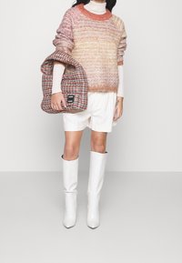 Gebreide trui in roze, oranje en crème met een geribbelde halslijn, gecombineerd met witte shorts en kniehoge, puntige witte laarzen. Draagt een geruite tas.