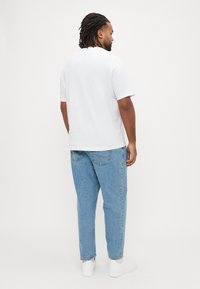 White short-sleeve t-shirt paired with light blue, loose-fitting jeans and white sneakers, viewed from the back.