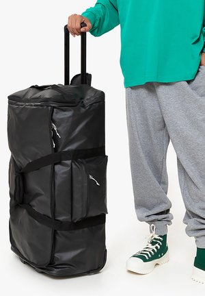 Zwarte rolduffelbag gemaakt van glanzend materiaal, met twee zijvakjes, zwarte banden, een uitschuifhandvat en een rechthoekige vorm.