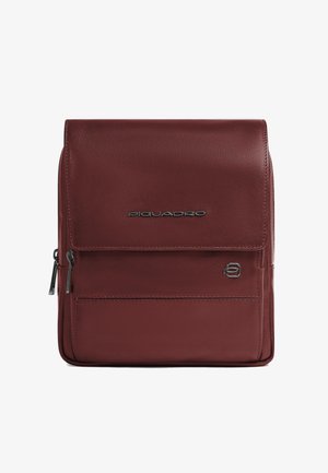 Sac en cuir bordeaux avec rabat avant, poche zippée et logo argenté. Texture lisse avec bords cousus et détails métalliques polis.