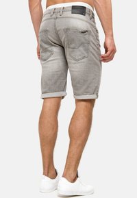 Grijze denim shorts met opgerolde omslagen, voorzien van twee achterzakken en een leren label op de tailleband. Gestyled met witte sneakers.