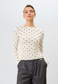 Lichtgekleurde blouse met lange mouwen en zwarte stippen, met een bootnek en een getailleerd ontwerp, in combinatie met grijze geplooide broek.