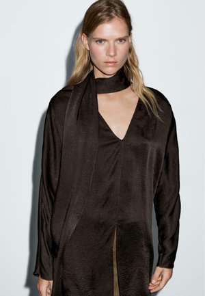 Blouse en tissu léger marron avec un col en V et des manches longues. Dotée d'une écharpe assortie nouée au cou et d'une fente sur le côté. Fini texturé.