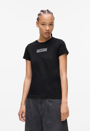 Zwarte katoenen t-shirt met korte mouwen, voorzien van een rechthoekig grijs logo op de borst. Eenvoudig, getailleerd ontwerp. Gestructureerde stof.