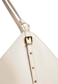 Lichte beige handtas met een driehoekige vorm, voorzien van een gouden gesp en gouden klinknagels langs de band. Gemaakt van soepel, getextureerd kunstleer.
