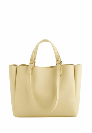 Kremowa torba typu tote wykonana ze skóry, wyposażona w dwie krótkie rączki oraz długi, regulowany pasek, o wyraźnie zarysowanej konstrukcji i złotych okuciach.