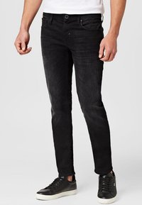 Jeans negros de corte ajustado, con un dise�ño clásico de cinco bolsillos, un ligero desgastado y combinados con zapatillas negras.