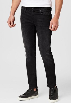 Jeans negros de corte ajustado, con un diseño clásico de cinco bolsillos, un ligero desgastado y combinados con zapatillas negras.