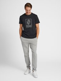 Zwarte katoenen t-shirt met een wit grafisch ontwerp, gecombineerd met lichtgrijze trainingsbroek en witte sneakers. Comfortabele, casual pasvorm.