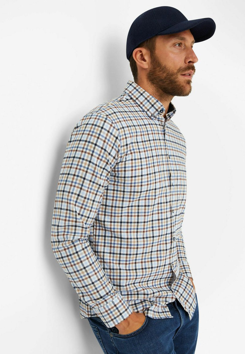 Kariertes Button-Up-Hemd in verschiedenen Blau-, Braun- und Weißtönen, mit langen Ärmeln und Kragen, kombiniert mit einer dunklen Baseballmütze.