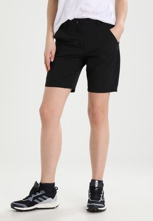 Person iført sorte knælange shorts, hvid t-shirt, sorte sokker og sorte løbesko mod en ensartet lys baggrund.