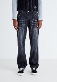 Mörk tvättade denimjeans med en lös passform, blekta detaljer och lätt slitningar, kombinerat med svarta och vita mönstrade sneakers.