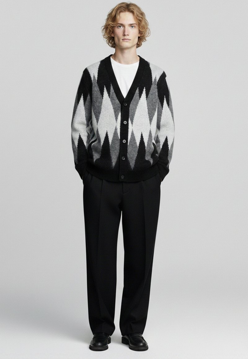 Cardigan nero e grigio con motivo a diamante, chiusura con bottoni e polsini a costine, abbinato a pantaloni neri e scarpe. Sotto, maglietta bianca semplice.