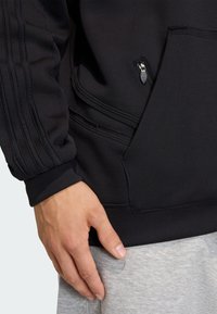 Čierna mikina so zipsovou vreckom, rebrovanými manžetami a bočným pruhom, s hladkou textúrou a priliehavým strihom.