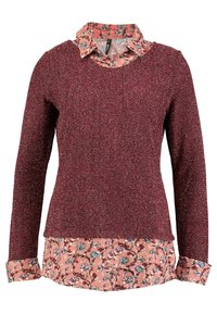 Maglione texturizzato marrone con maniche lunghe indossato sopra una camicia a stampa floreale rosa. Presenta un collo tondo e polsini a contrasto.