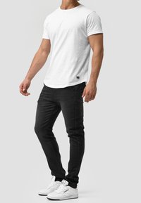 T-shirt blanc basique à manches courtes, associé à un jean slim noir. Complété par des baskets blanches avec des accents de marque discrets.