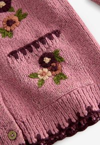Pink knitted sweater sleeve with a pocket decorated with embroidered flowers in green, cream, mauve, and burgundy yarn.