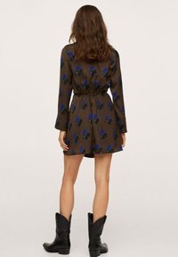 Vestido floral marrón con mangas largas, cintura ajustable con cordón y estampado de flores azules. Estilizado con botas de vaquero negras. Longitud hasta medio muslo, fabricado en tejido suave.