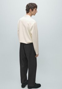Jasnokremowa koszula z długim rękawem w połączeniu z ciemnymi, luźnymi spodniami, charakteryzująca się prostym wzorem i minimalistycznym wyglądem, widziana od tyłu.