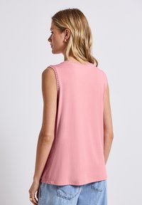 Haut rose sans manches avec un col rond orné de coutures décoratives, en tissu doux et à coupe décontractée, associé à un jean en denim clair.