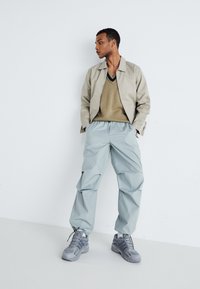 Light grey baggy trousers, beige v-neck sweater, and a light beige jacket. Styled with grey sneakers, featuring subtle design details.