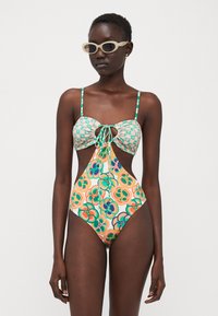 Bikini avec un haut à nouer à l'avant ; motif floral vert et orange ; côtés découpés ; fines bretelles ; matériau lisse ; lunettes de soleil assorties.