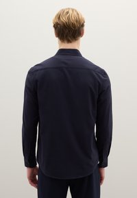 Navyblauw overhemd met lange mouwen, voorzien van een klassieke kraag, knoopmanchetten en een gladde textuur. Getailleerde pasvorm met een afgeronde zoom aan de achterkant.