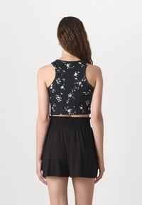 Top corto floreale nero con texture a coste. Presenta un collo rotondo e un design senza maniche. Abbinato a pantaloni corti neri con vita elastica.