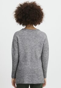 Pull en tricot gris à coupe décontractée, avec un ourlet côtelé et des manches longues. Texture douce, col rond et un dos légèrement plus long.