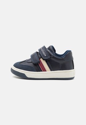 Navyblå børnesneaker med to velcrobånd, hvid sål og røde og hvide siderstriber, set fra højre side.