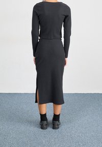 Svart ribbad tvådelad set med en kortärmad topp och en midi kjol med sidofickor. Modellen bär svarta skor och strumpor.