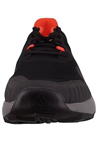 Chaussure de sport noire avec des accents orange, dessus en mesh, languette rembourrée et semelle texturée contrastante, avec le logo Adidas sur le talon.