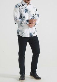 Chemise blanche avec des motifs floraux bleus, à manches longues et à boutons sur le devant. Associée à un pantalon noir et des chaussures noires.