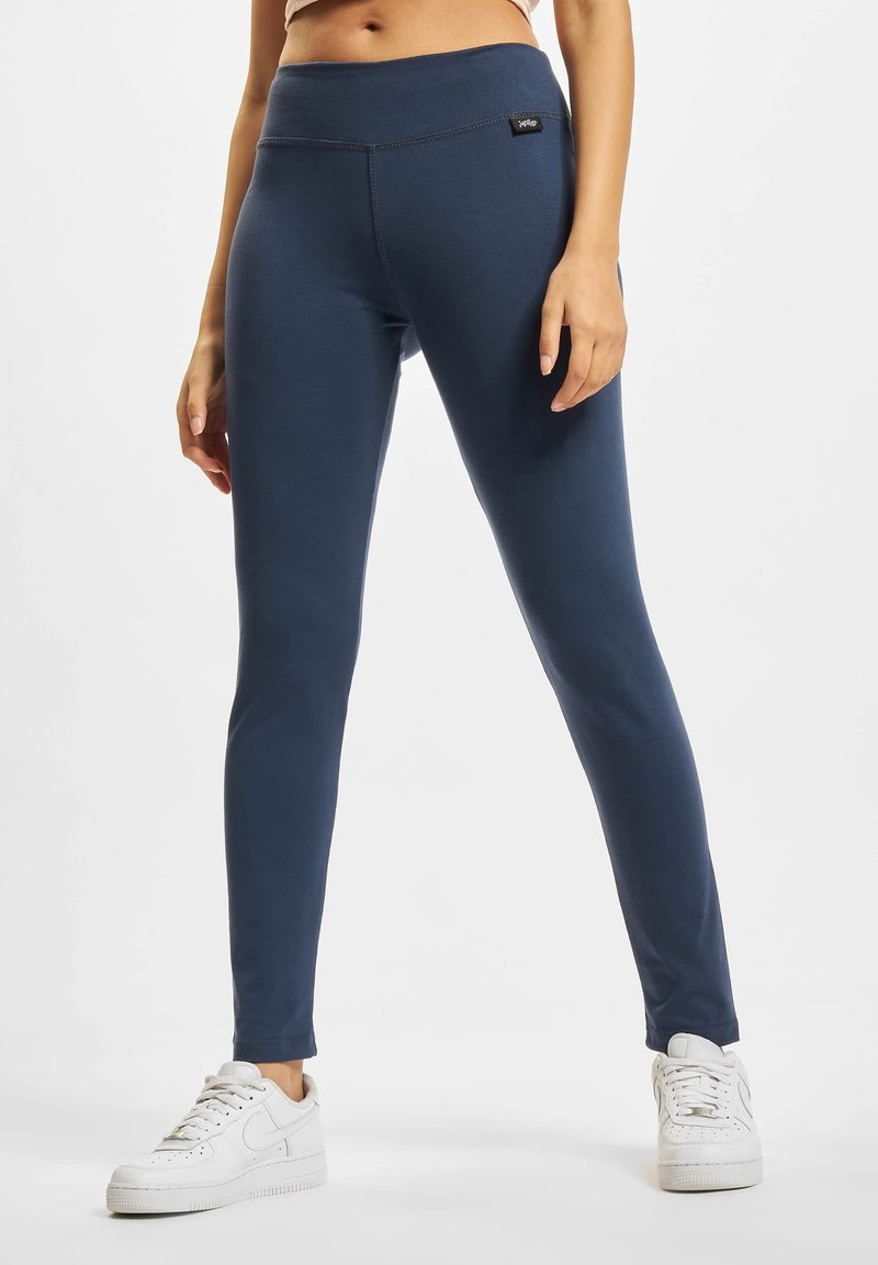 Marineblauwe leggings van rekbaar fabric met een brede tailleband en een klein label aan de voorkant, gecombineerd met witte sneakers.
