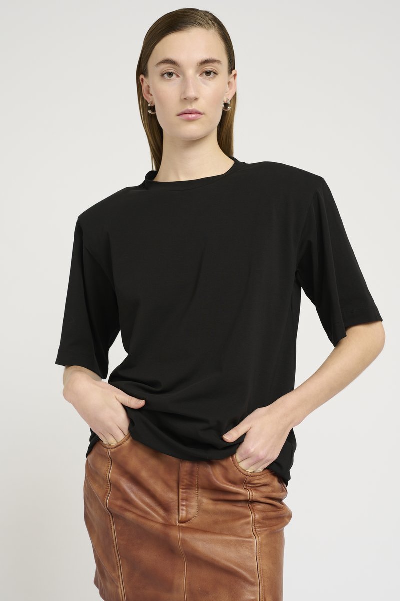 T-shirt nera a maniche corte con una vestibilità relax e scollo rotondo, abbinata a una gonna di pelle marrone con tasche frontali e una texture liscia.