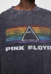 Sudadera gris de gran tamaño con un diseño gráfico desvanecido que presenta un prisma y rayas de arcoíris sobre el texto "PINK FLOYD" en blanco.