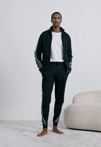 Čierna športová súprava s šedými akcentmi a bielymi bočnými pruhmi, pozostávajúca z bundičky so zapínaním na zips a úzkych teplákov, vyrobená z jemnej látky.