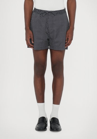 Black shorts with a white polka dot pattern, elastic waistband, and side slits, paired with white socks and black loafers.