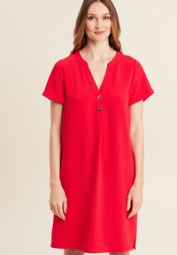 Rotes Kurzarmkleid mit V-Ausschnitt, ausgestattet mit zwei Knopfdetails und einem lockeren Schnitt. Glatter Stoff mit seitlichen Schlitzöffnungen.