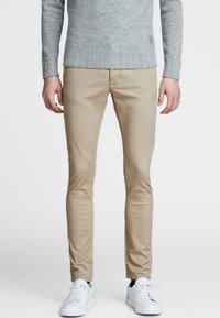 Chinos beige hechos de algodón, con un diseño de corte ajustado. Combinados con un suéter gris texturizado y zapatillas blancas.