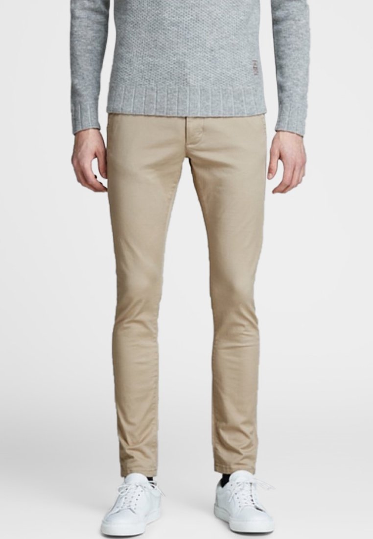 Chinos beige hechos de algodón, con un diseño de corte ajustado. Combinados con un suéter gris texturizado y zapatillas blancas.