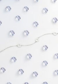 Bracciale a catena argentata con anelli esagonali, collocato tra pietre circolari simili a cristalli, il tutto su uno sfondo bianco.