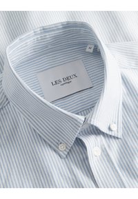 Gestreepte blauwe en witte katoenen shirt met een button-down kraag, voorzien van witte knopen en een label met de tekst "LES DEUX copenhagen."