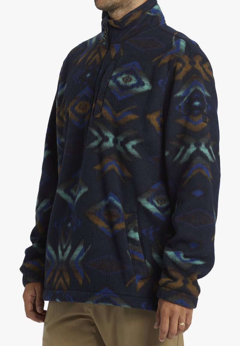 Marineblauer Fleece-Pullover mit geometrischen Mustern in Blau, Türkis und Braun. Mit einem Halsriegel mit halber Reißverschlussöffnung und einer Seitentasche. Strukturierter Stoff.