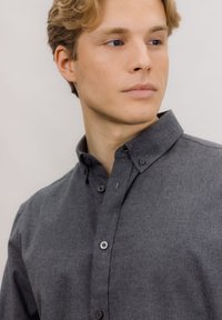 Mørkegrå skjorte med knapper foran, spredt krage, teksturert stoff, og synlige knapper, som viser en avslappet stil.