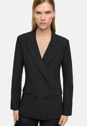 Czarna marynarka dwurzędowa z ostro zakończonymi klapami, dwoma przednimi kieszeniami i fakturowanym materiałem. Posiada dwa duże zapięcia na guziki.