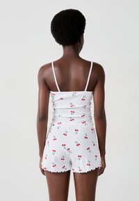 Witte korte set bestaande uit een tanktop met dunne banden en shorts, beide versierd met een kersenpatroon en golvende randen.